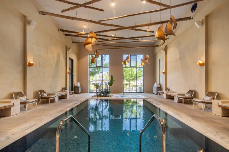 Heated indoor spa pool for adults at Ayala by Isrotel Collection, loungers along the sides and tall windows